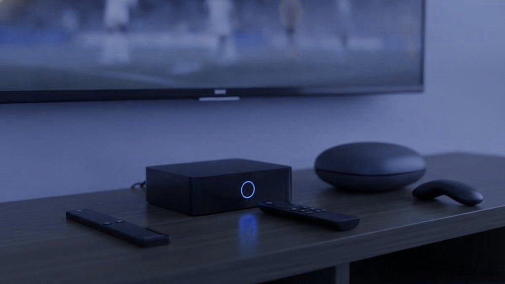 A streaming stick, a set-top box and a round streaming box with their remotes on a TV console