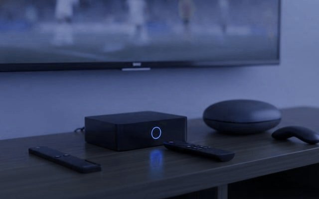 A streaming stick, a set-top box and a round streaming box with their remotes on a TV console